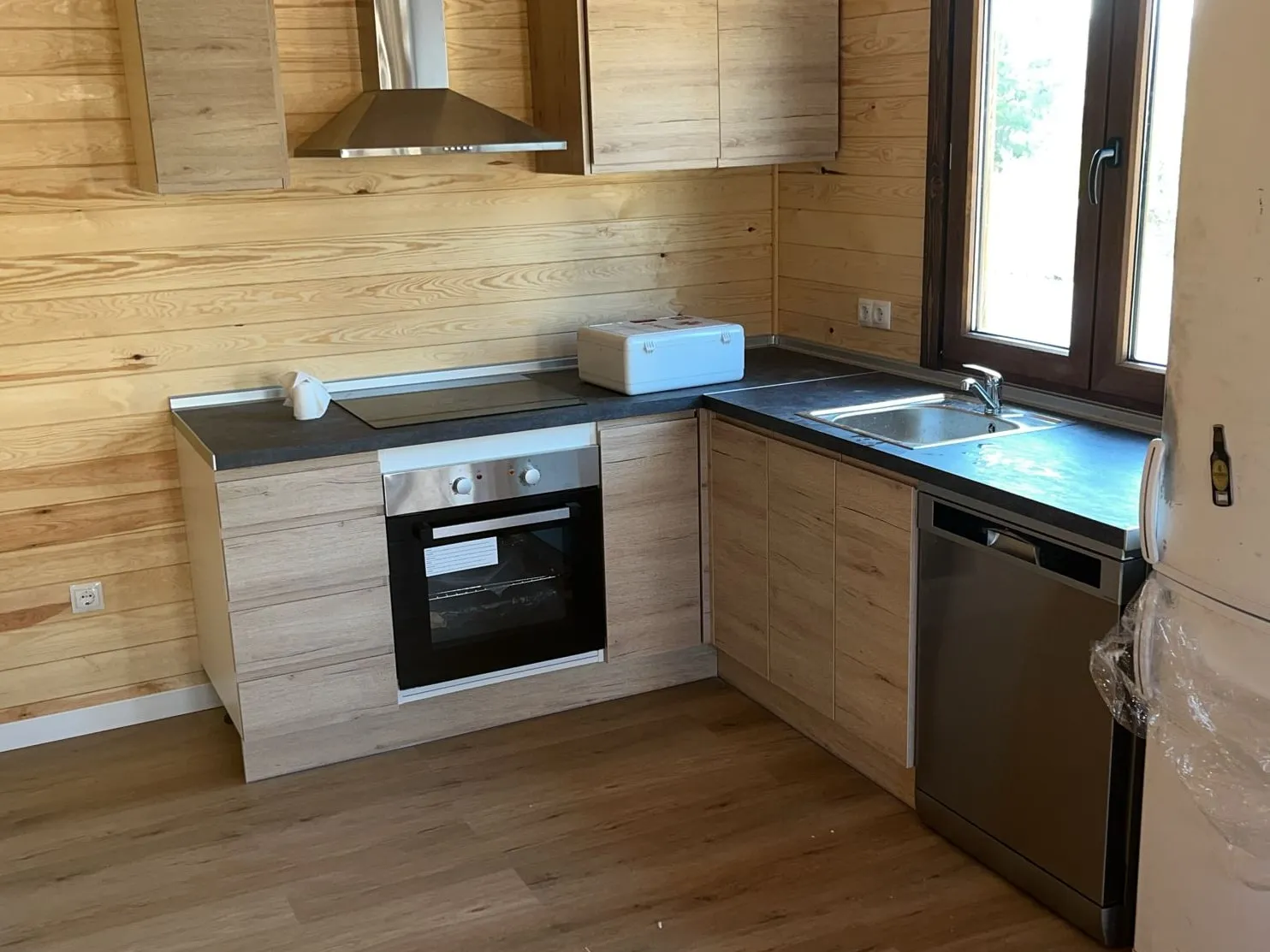 La misma cocina terminada, con encimera oscura, placa, horno, fregadero y lavavajillas