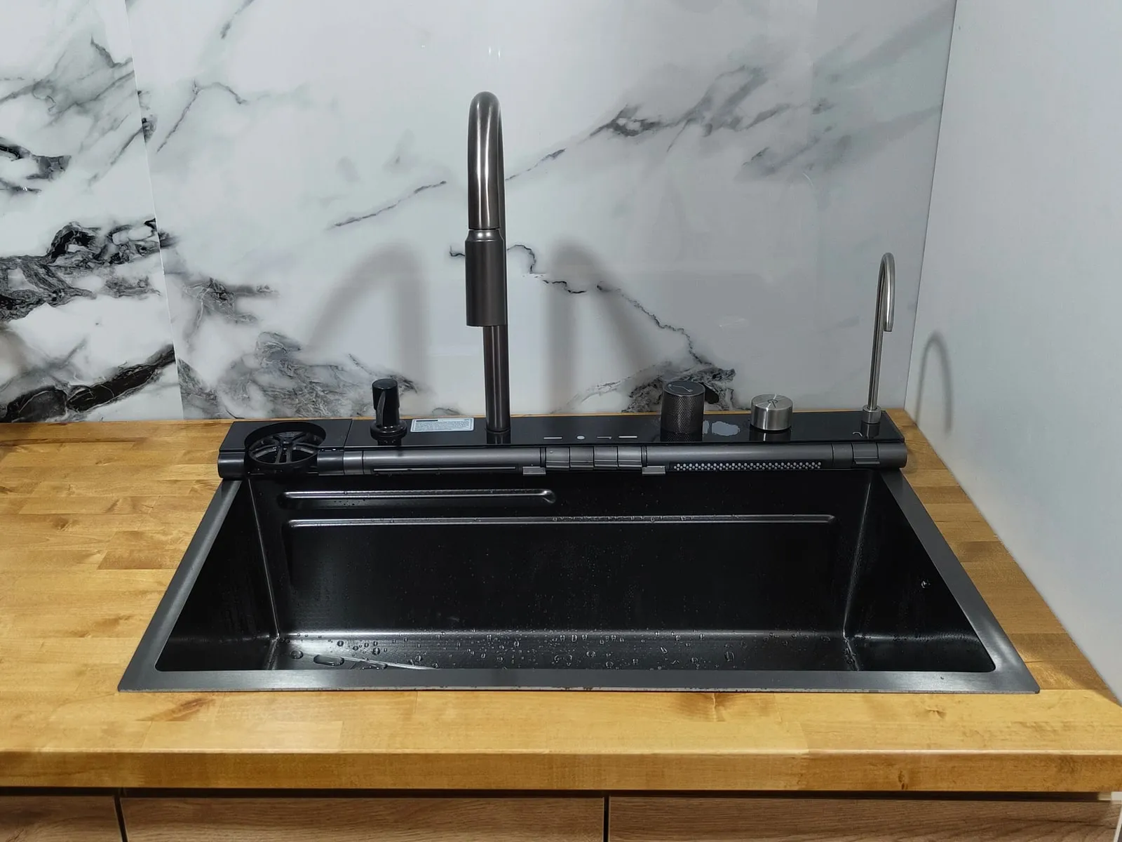 Fregadero negro con grifo extraíble en una encimera de madera, con frontal blanco efecto mármol