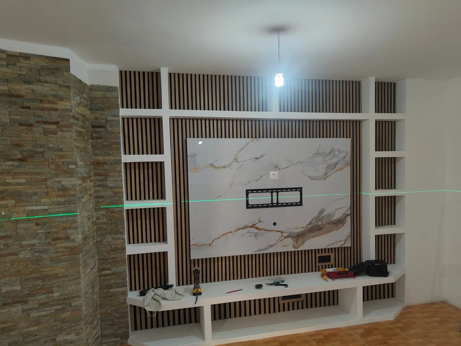 El mismo salón con el mueble terminado: estanterías de pladur, listones de madera, panel efecto mármol y columna de piedra