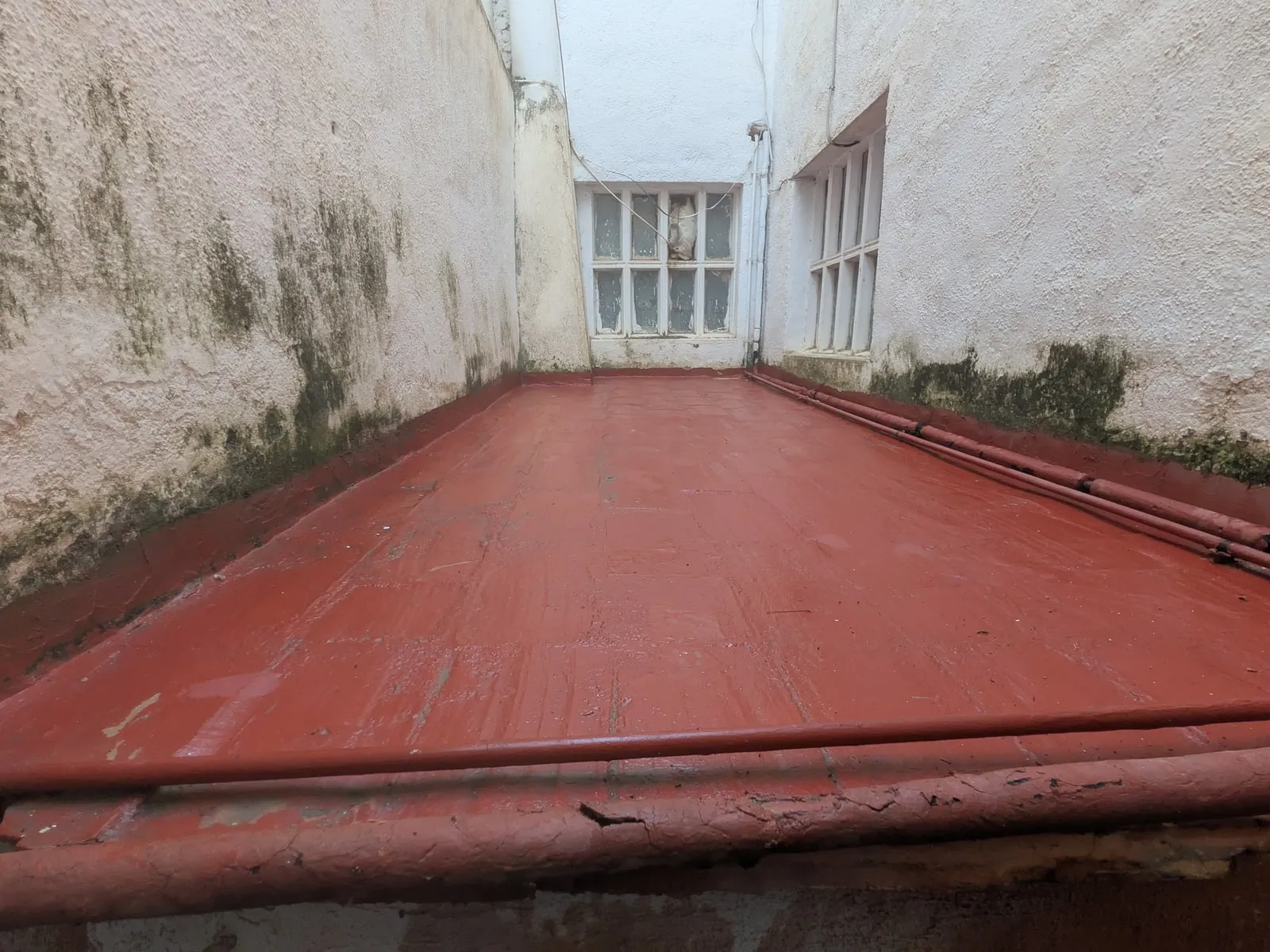 Patio de luces con el suelo impermeabilizado en rojo entre dos paredes