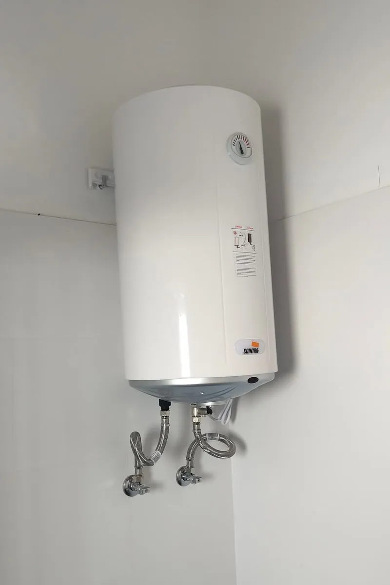 Termo eléctrico blanco colgado en la pared, con latiguillos y llaves de paso